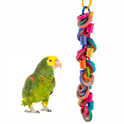 A large parrot standing next to a colorful hanging toy consisting of multiple shredded pieces.