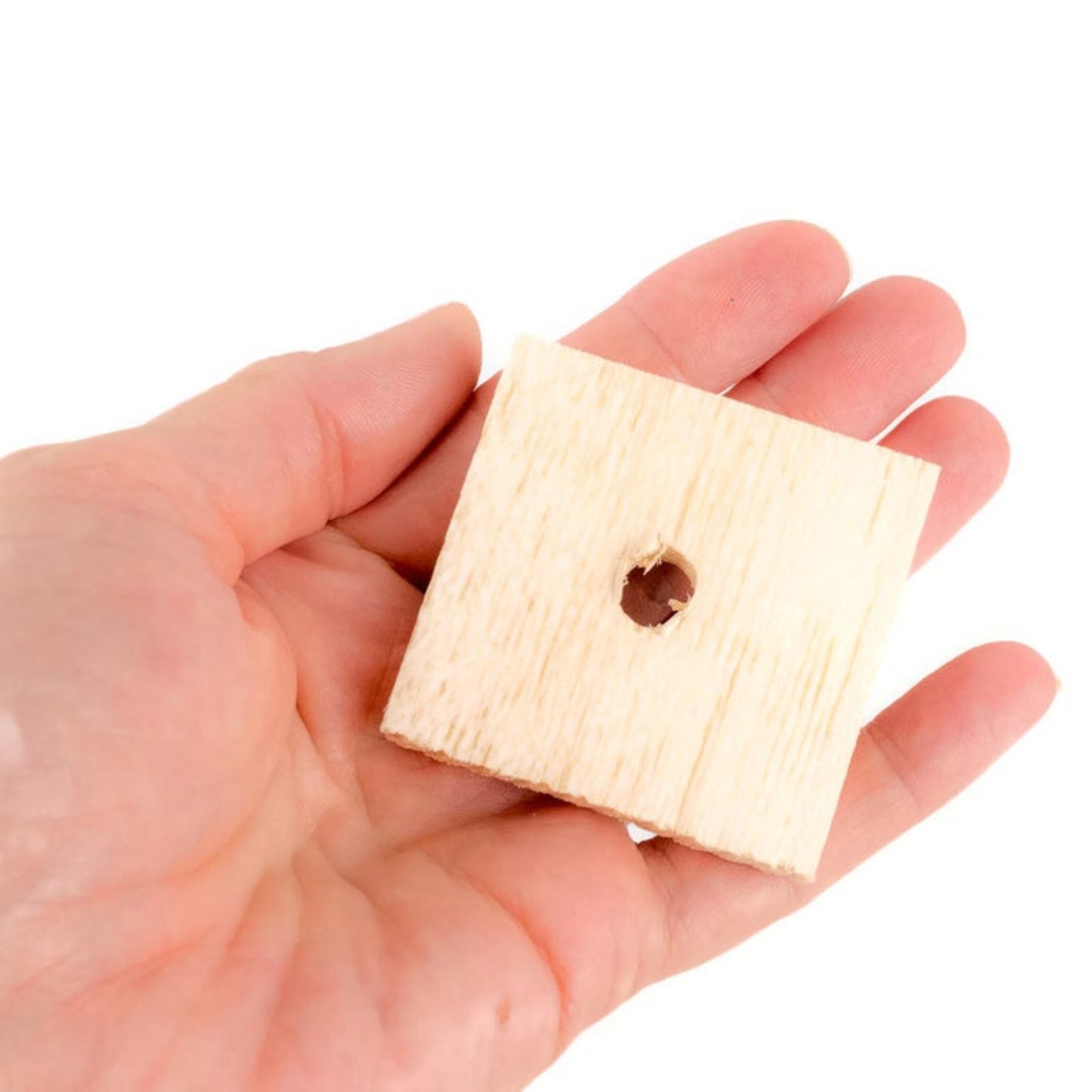 Hand holding a small square wooden block with a hole on a white background