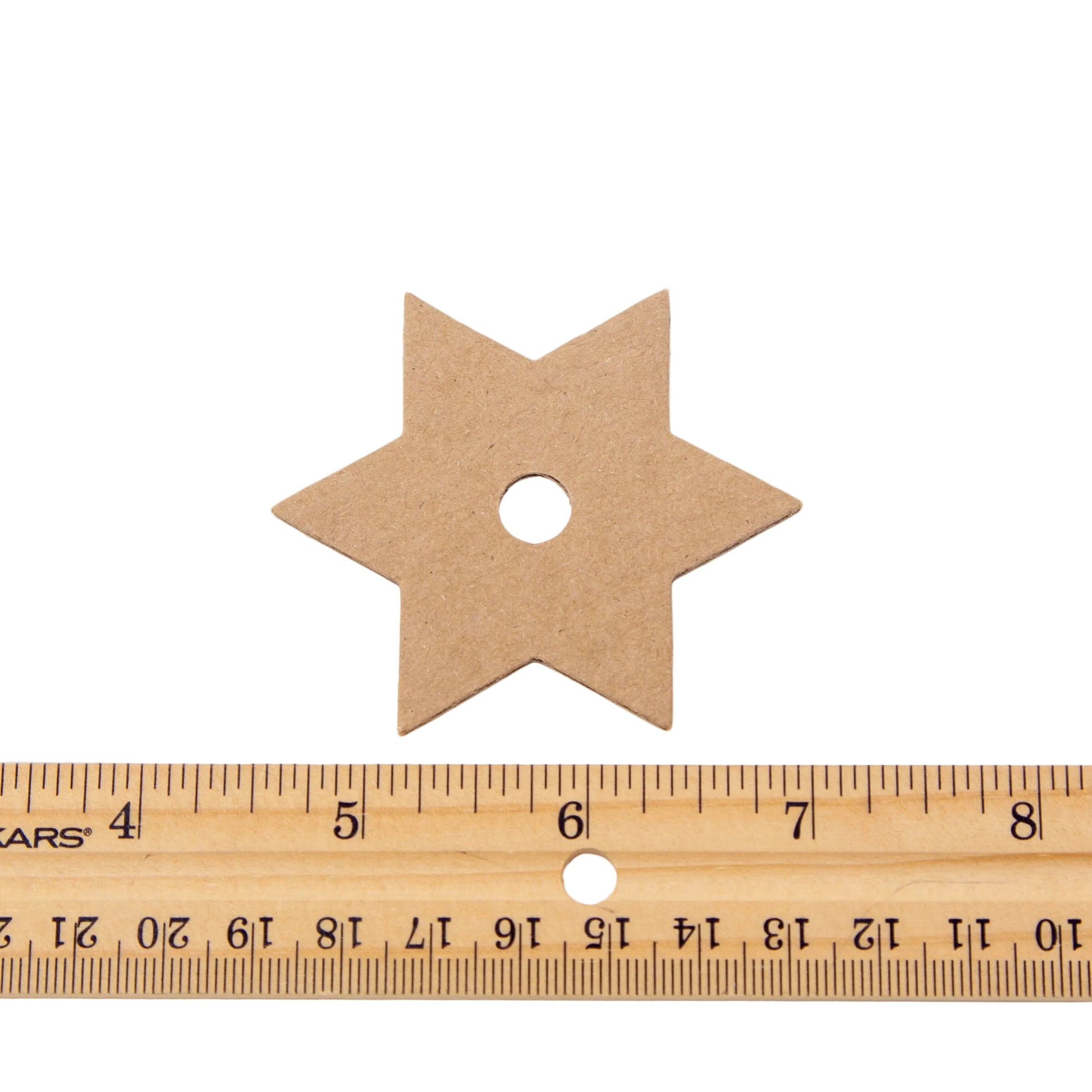 A six-pointed star-shaped piece of kraft cardboard with a central hole, shown above a wooden ruler for scale on a white background.
