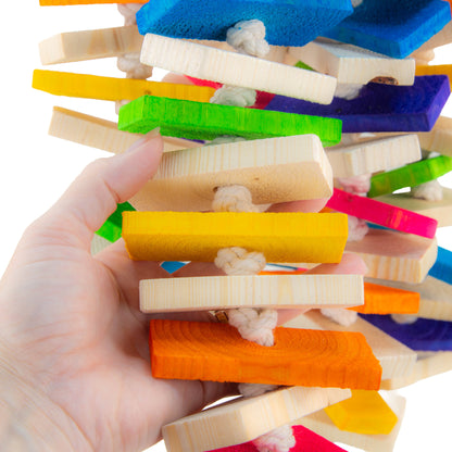 A hand holding a colorful bird toy made of layered wooden blocks connected by white rope, shown against a white background.