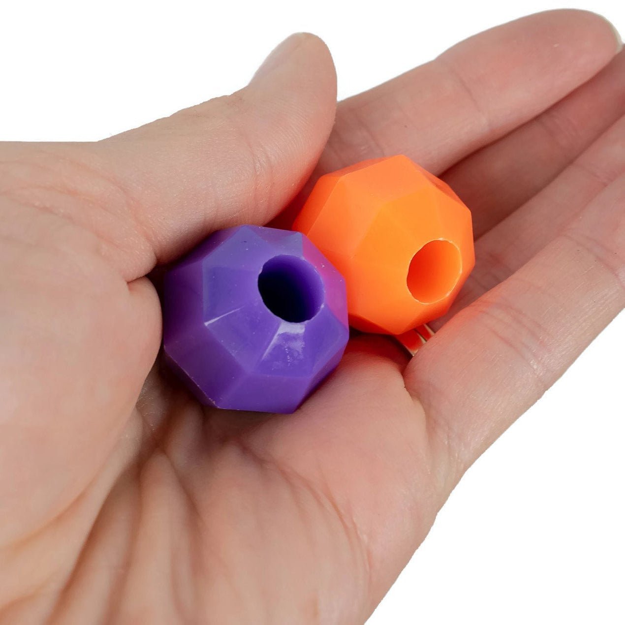 Hand holding two octagonal beads, one purple and one orange, on a white background.