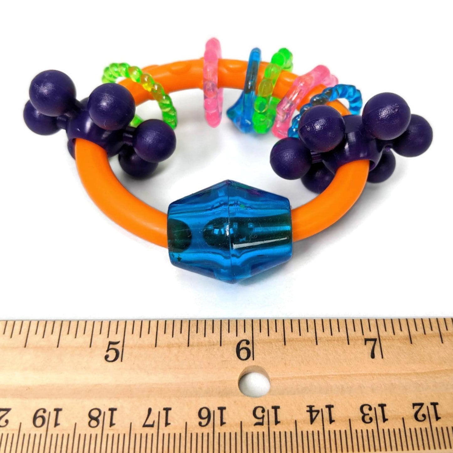 Colorful parrot foot toy with a ruler for scale on a white background