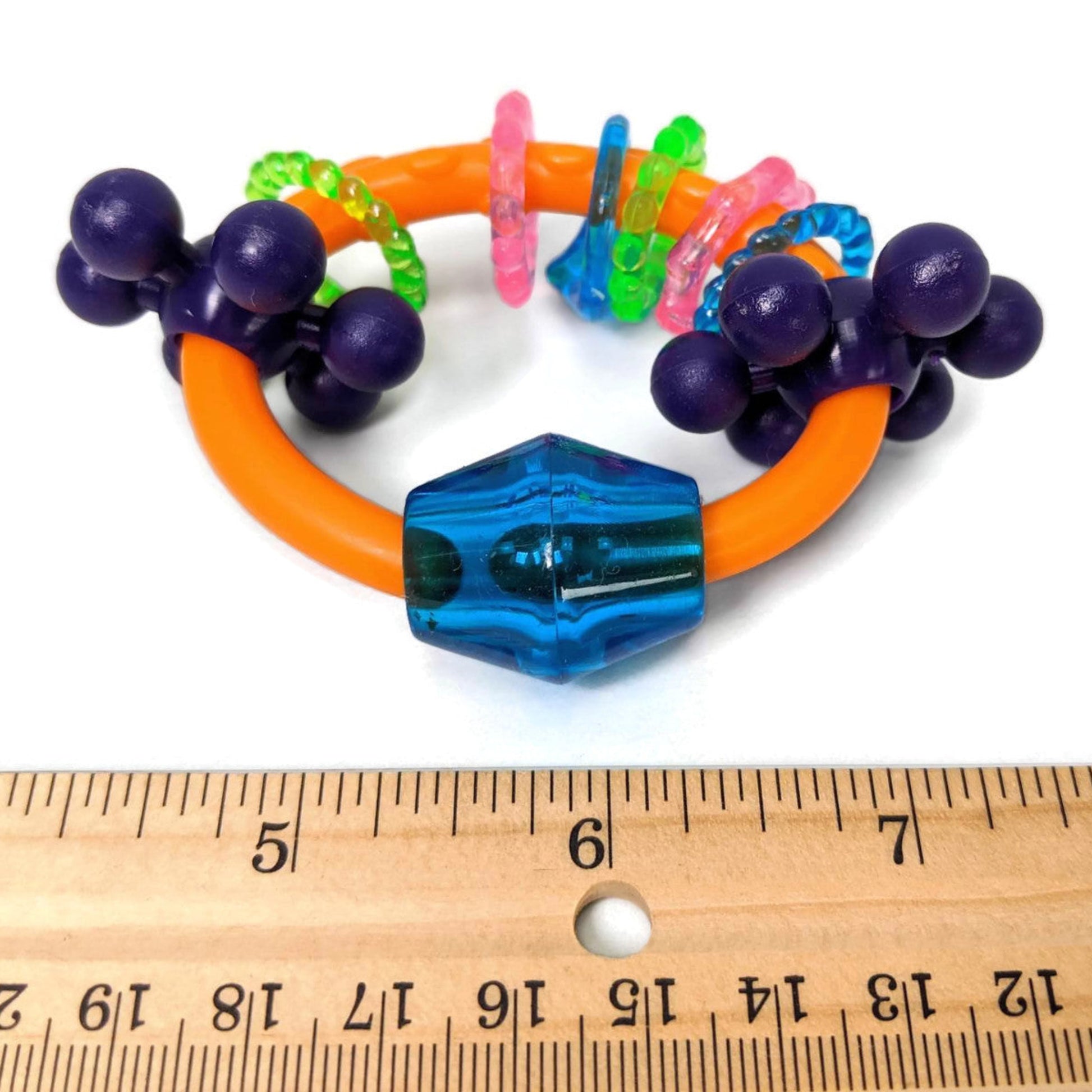 Colorful parrot foot toy with a ruler for scale on a white background